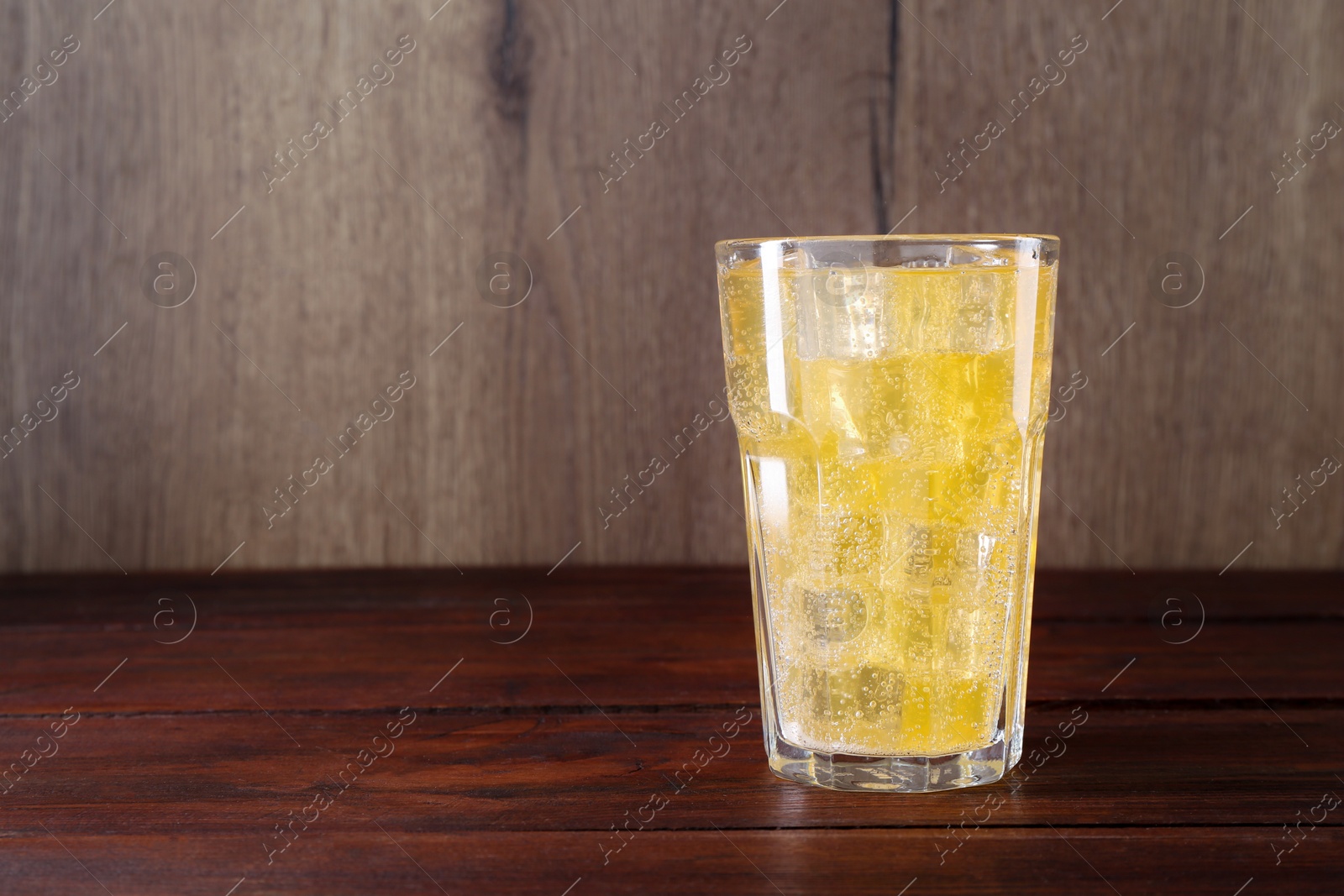 Photo of Sweet soda water with ice cubes in glass on wooden table, space for text