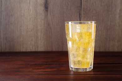 Photo of Sweet soda water with ice cubes in glass on wooden table, space for text