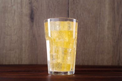 Photo of Sweet soda water with ice cubes in glass on wooden table