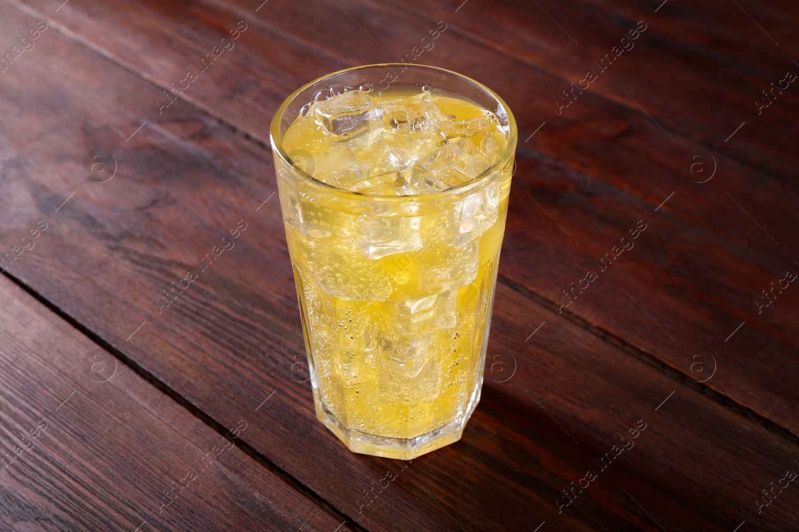 Photo of Sweet soda water with ice cubes in glass on wooden table