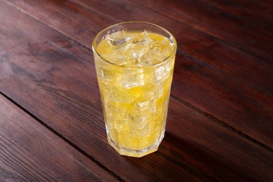 Photo of Sweet soda water with ice cubes in glass on wooden table