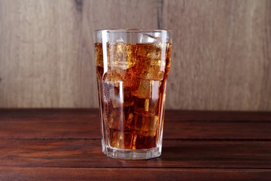 Photo of Sweet soda water with ice cubes in glass on wooden table