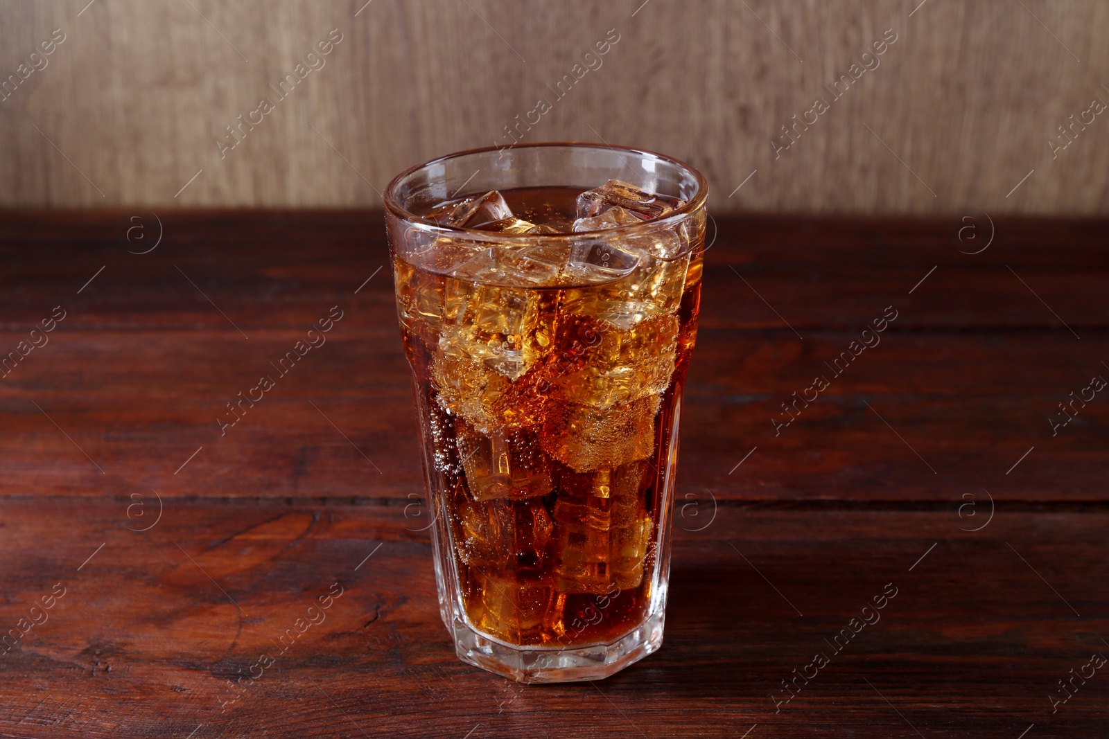 Photo of Sweet soda water with ice cubes in glass on wooden table