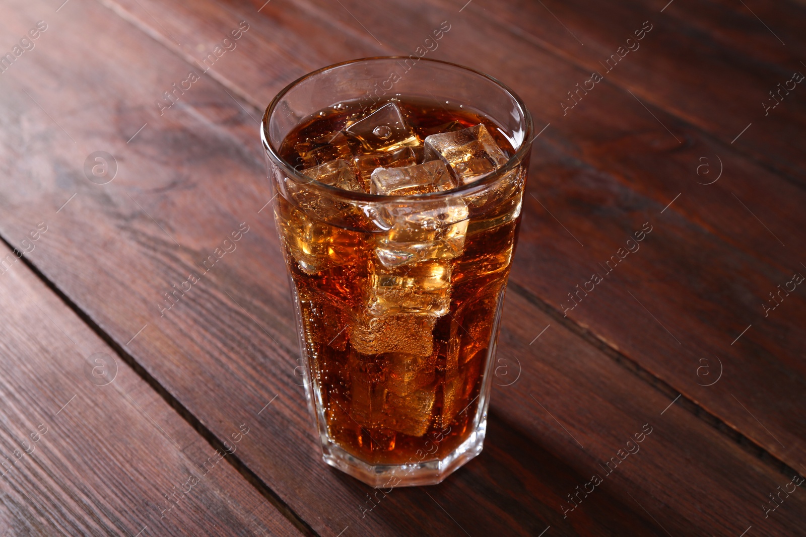 Photo of Sweet soda water with ice cubes in glass on wooden table, closeup