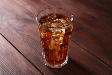 Photo of Sweet soda water with ice cubes in glass on wooden table, closeup