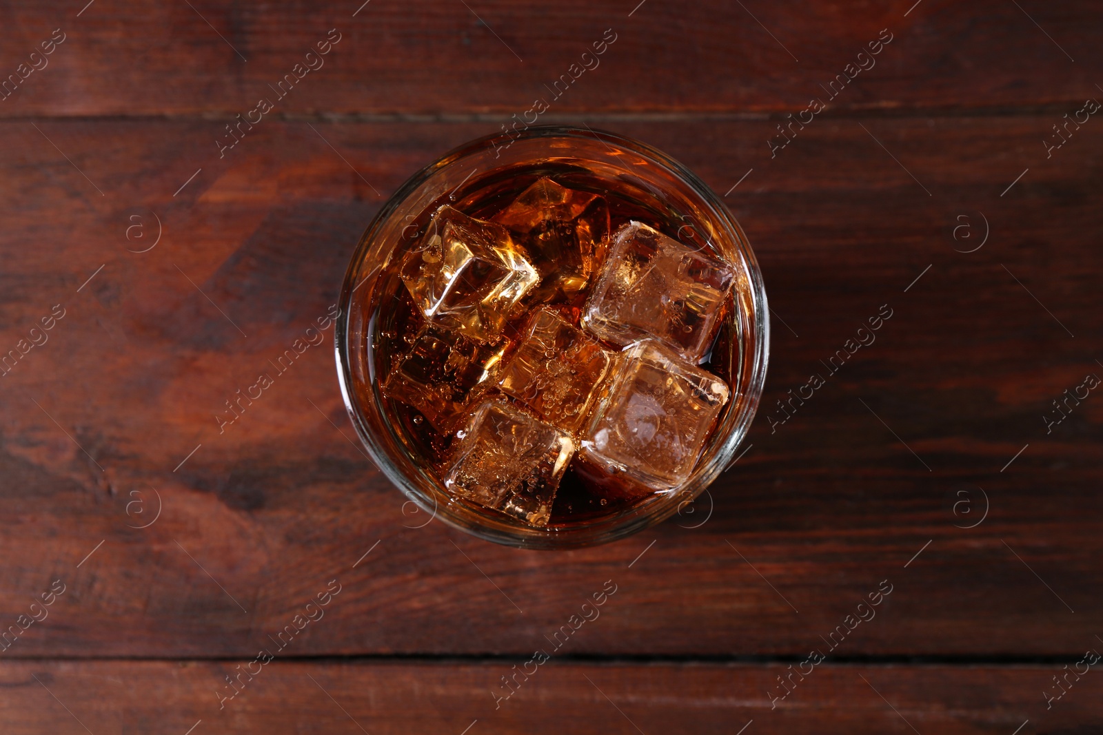 Photo of Sweet soda water with ice cubes in glass on wooden table, top view