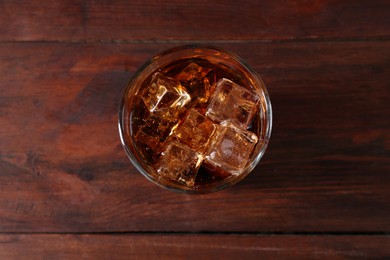 Photo of Sweet soda water with ice cubes in glass on wooden table, top view