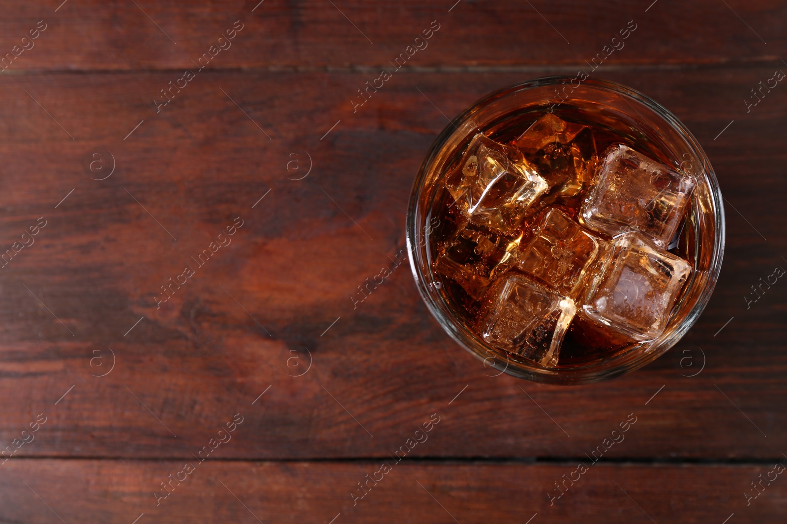 Photo of Sweet soda water with ice cubes in glass on wooden table, top view. Space for text