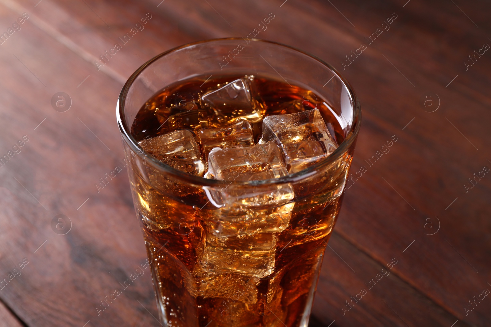 Photo of Sweet soda water with ice cubes in glass on wooden table, closeup