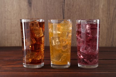 Photo of Refreshing soda water of different flavors with ice cubes in glasses on wooden table