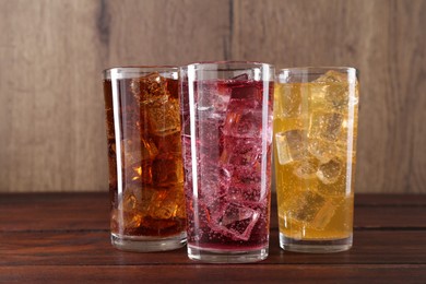 Photo of Refreshing soda water of different flavors with ice cubes in glasses on wooden table