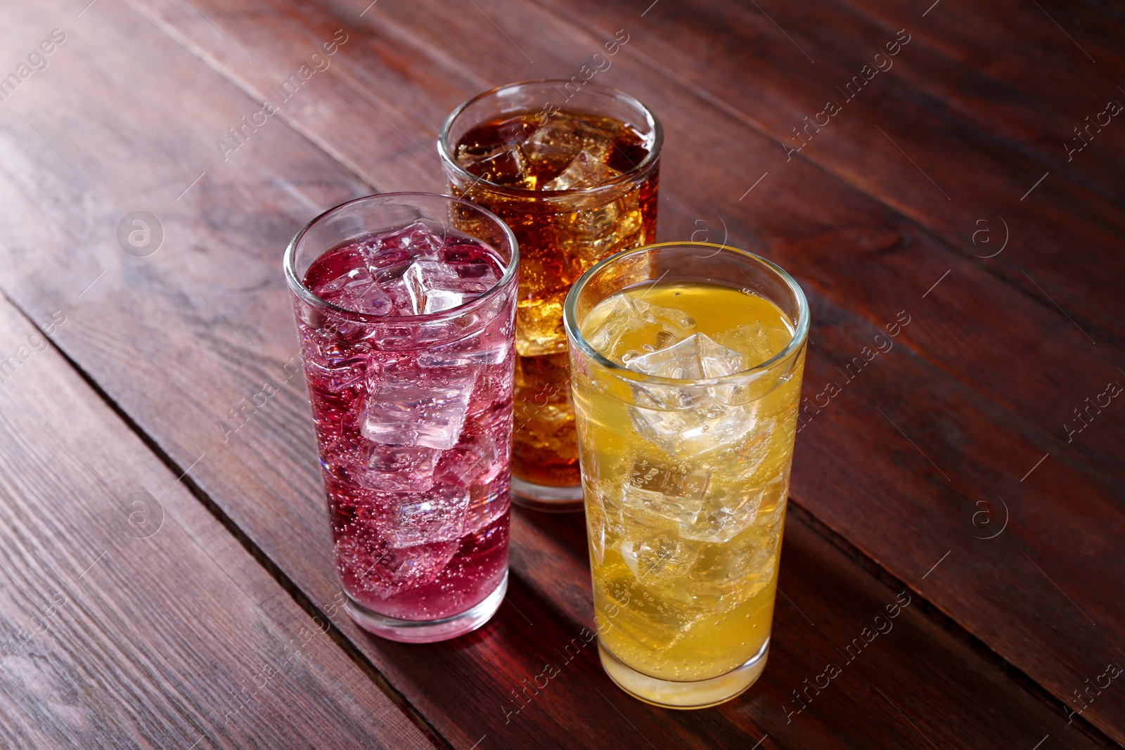 Photo of Refreshing soda water of different flavors with ice cubes in glasses on wooden table, closeup