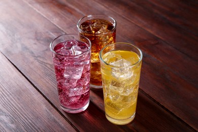 Photo of Refreshing soda water of different flavors with ice cubes in glasses on wooden table, closeup