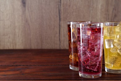 Photo of Refreshing soda water of different flavors with ice cubes in glasses on wooden table. Space for text