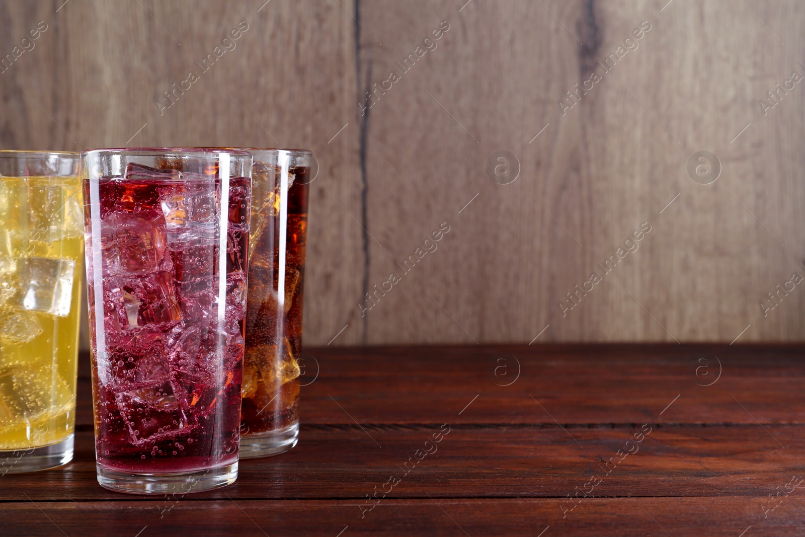 Photo of Refreshing soda water of different flavors with ice cubes in glasses on wooden table. Space for text