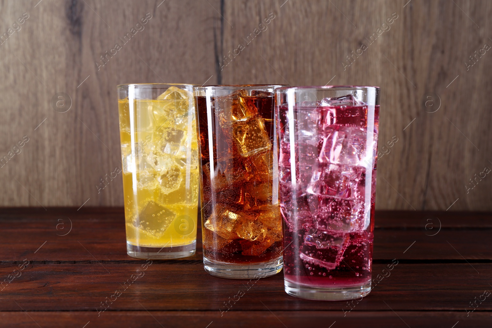 Photo of Refreshing soda water of different flavors with ice cubes in glasses on wooden table