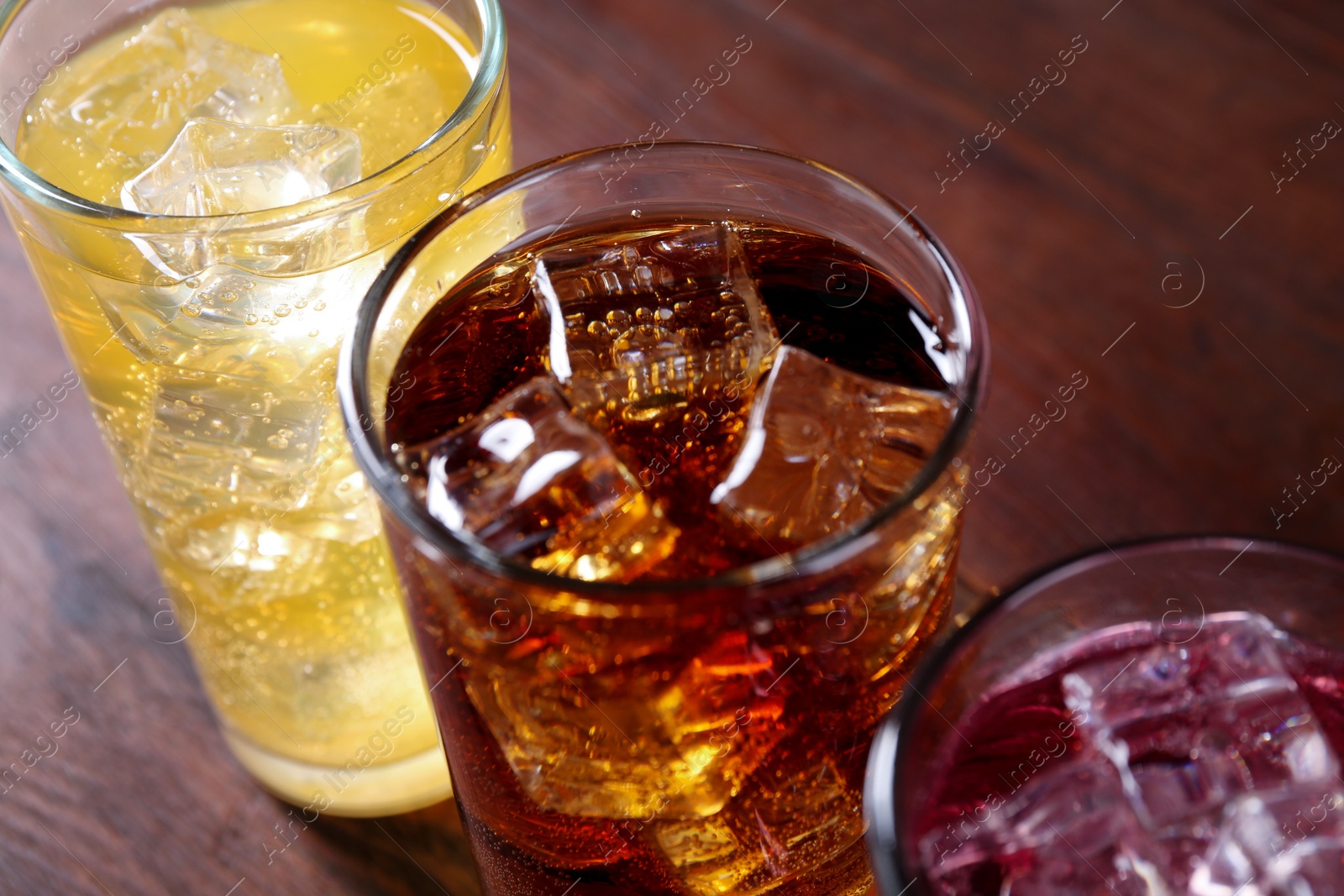 Photo of Refreshing soda water of different flavors with ice cubes in glasses on wooden table, closeup