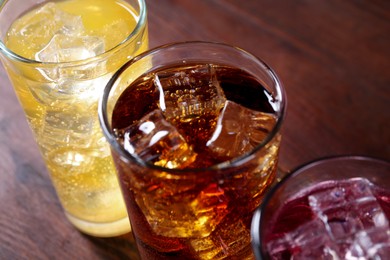 Photo of Refreshing soda water of different flavors with ice cubes in glasses on wooden table, closeup