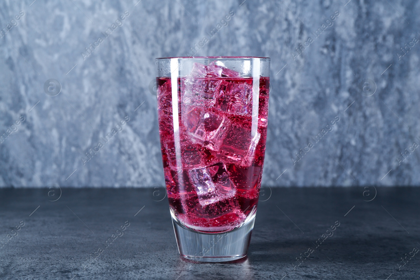 Photo of Sweet soda water with ice cubes in glass on grey table