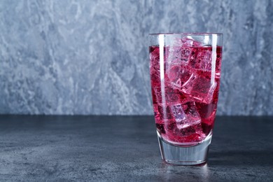 Photo of Sweet soda water with ice cubes in glass on grey table, space for text