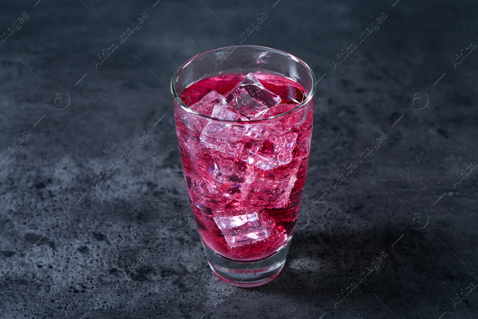 Photo of Sweet soda water with ice cubes in glass on grey table, closeup