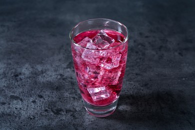 Photo of Sweet soda water with ice cubes in glass on grey table, closeup