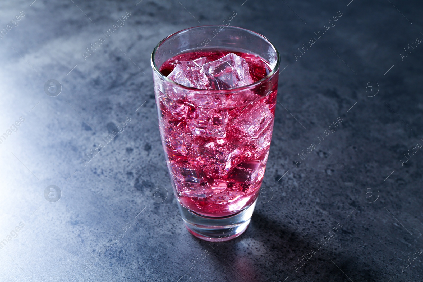 Photo of Sweet soda water with ice cubes in glass on grey table