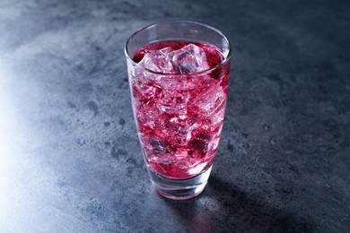 Photo of Sweet soda water with ice cubes in glass on grey table