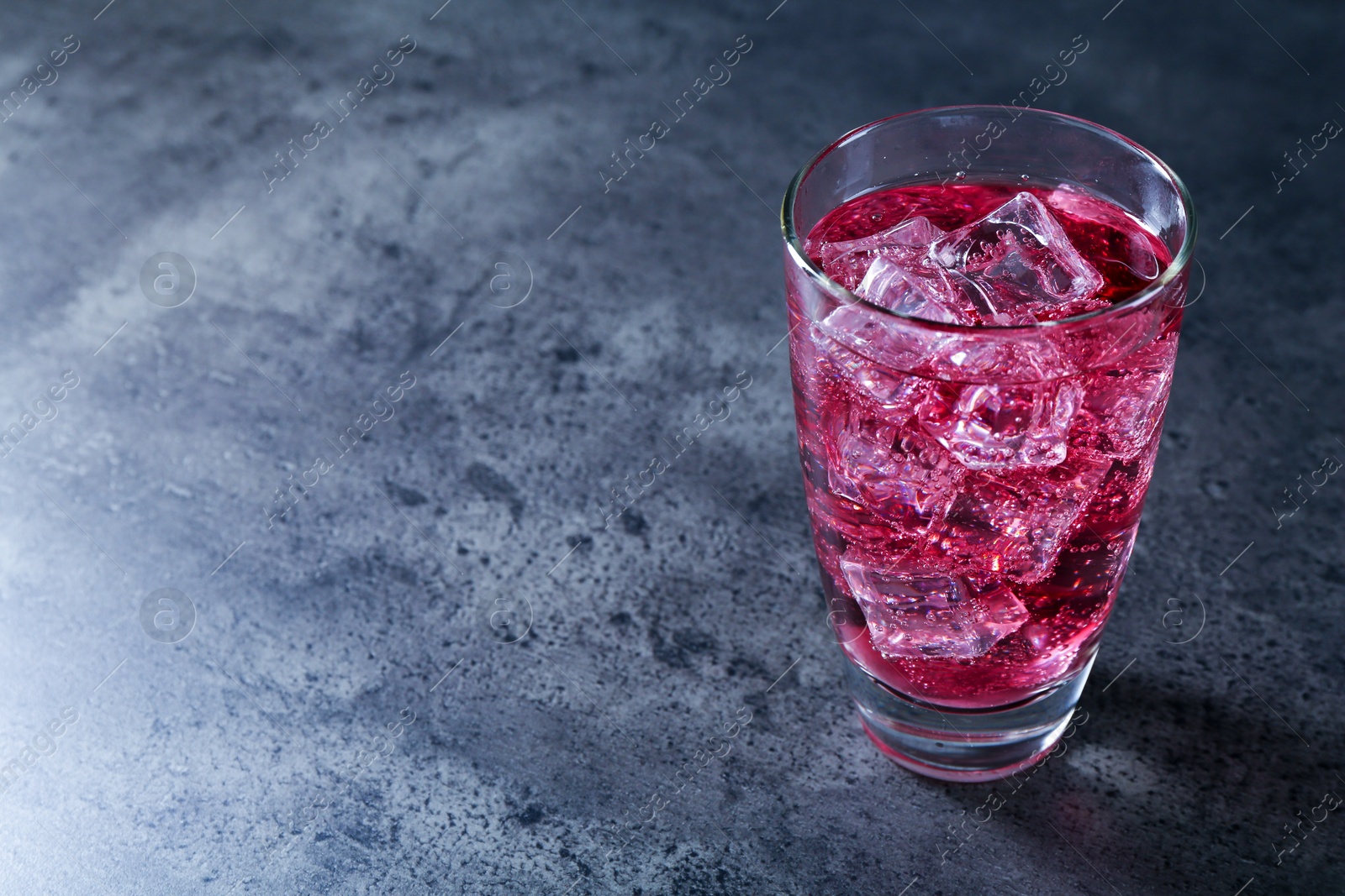 Photo of Sweet soda water with ice cubes in glass on grey table, space for text