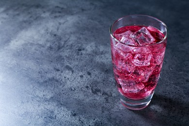 Photo of Sweet soda water with ice cubes in glass on grey table, space for text