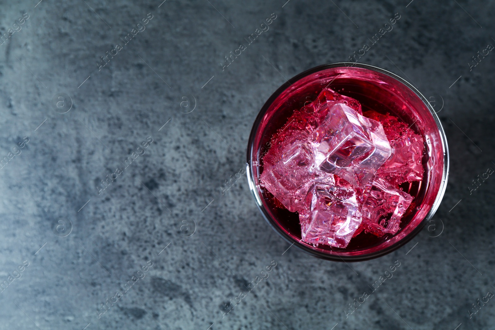 Photo of Sweet soda water with ice cubes in glass on grey table, top view. Space for text