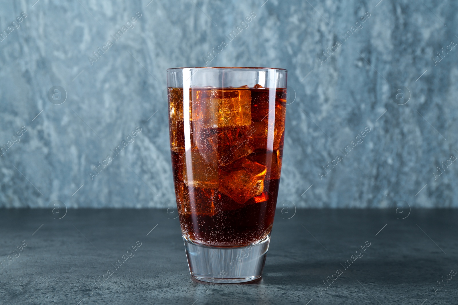 Photo of Sweet soda water with ice cubes in glass on grey table