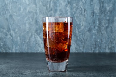 Photo of Sweet soda water with ice cubes in glass on grey table