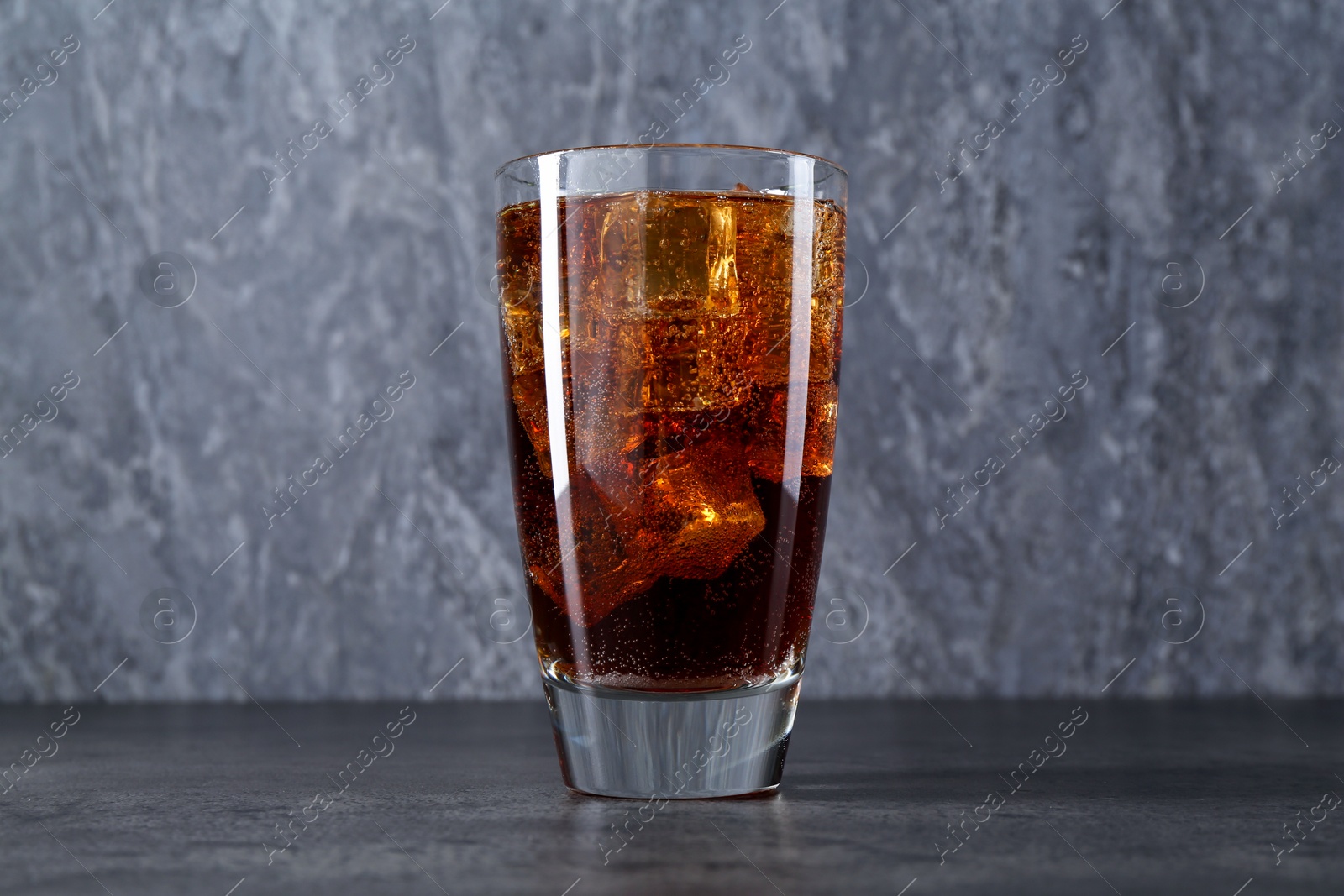 Photo of Sweet soda water with ice cubes in glass on grey table