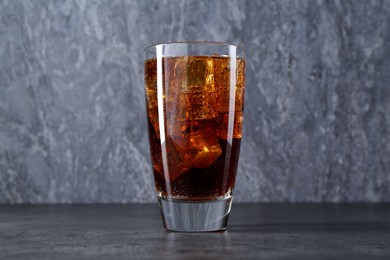 Photo of Sweet soda water with ice cubes in glass on grey table