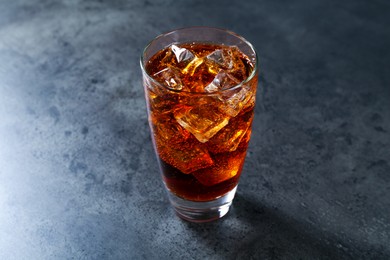 Photo of Sweet soda water with ice cubes in glass on grey table, closeup