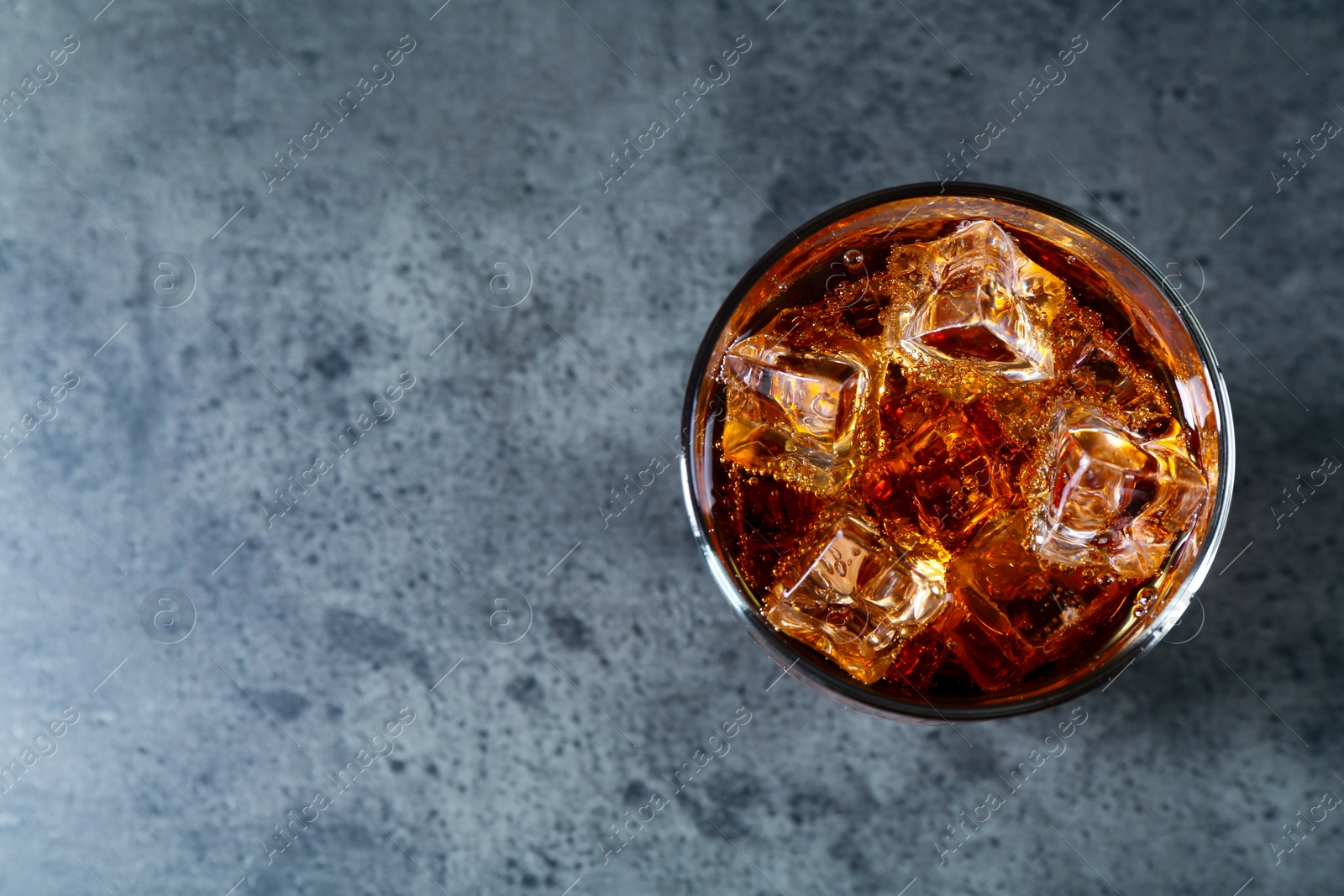 Photo of Sweet soda water with ice cubes in glass on grey table, top view. Space for text