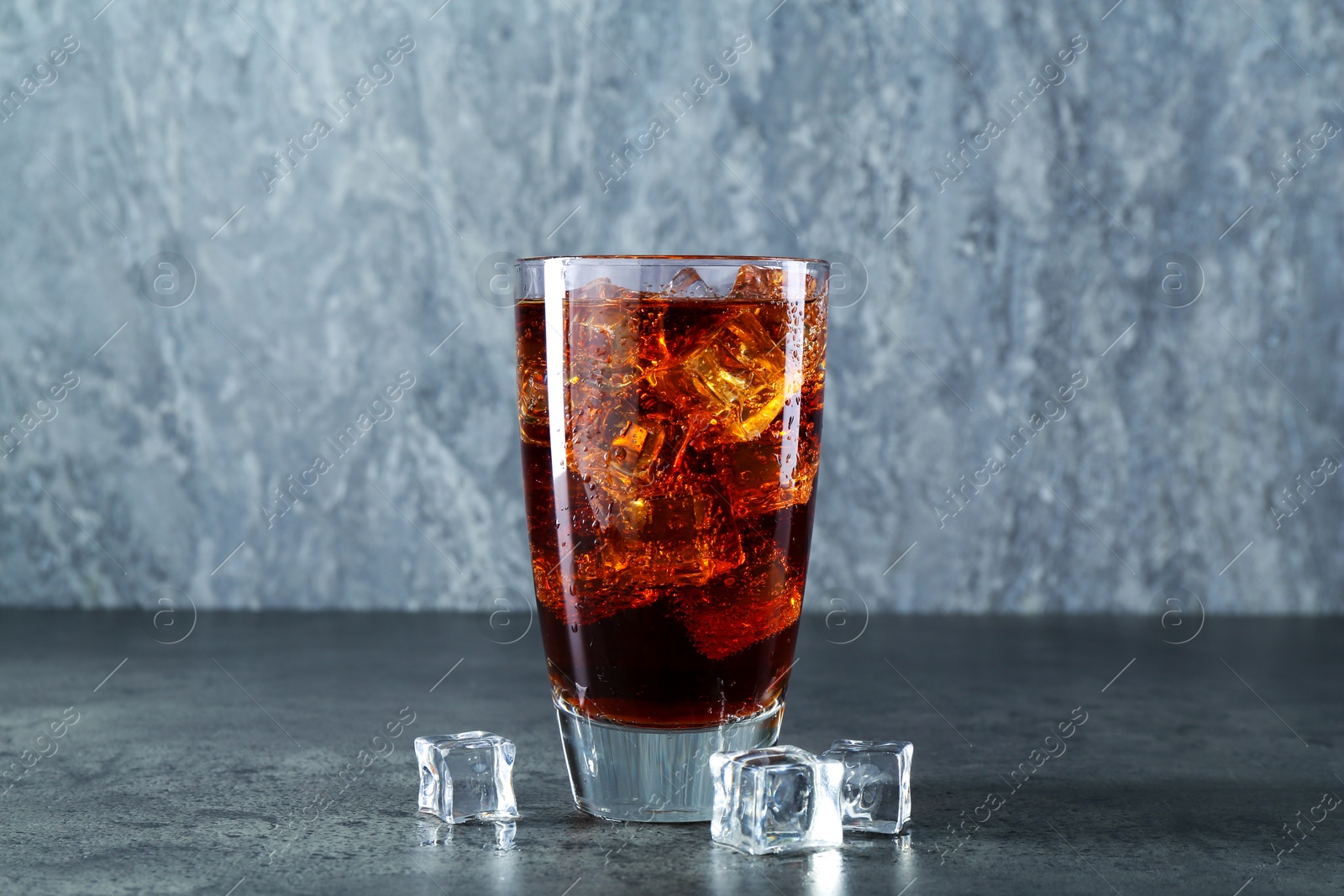 Photo of Sweet soda water in glass with ice cubes on grey table