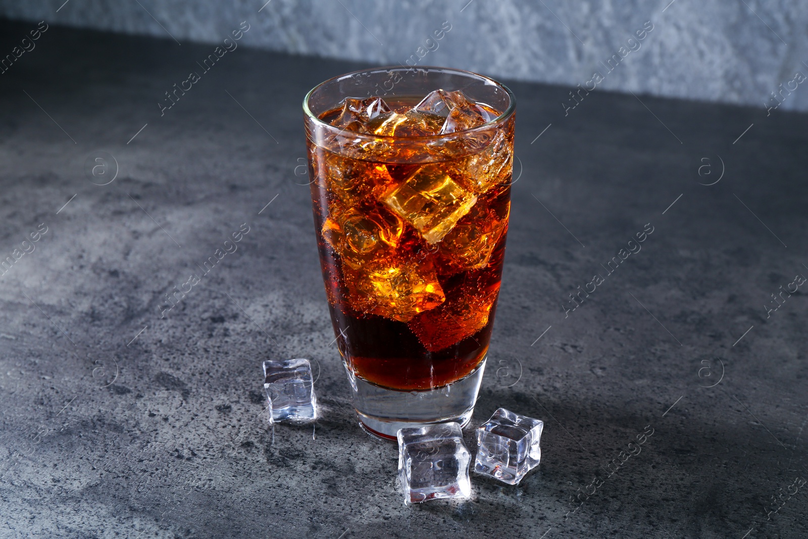 Photo of Sweet soda water in glass with ice cubes on grey table