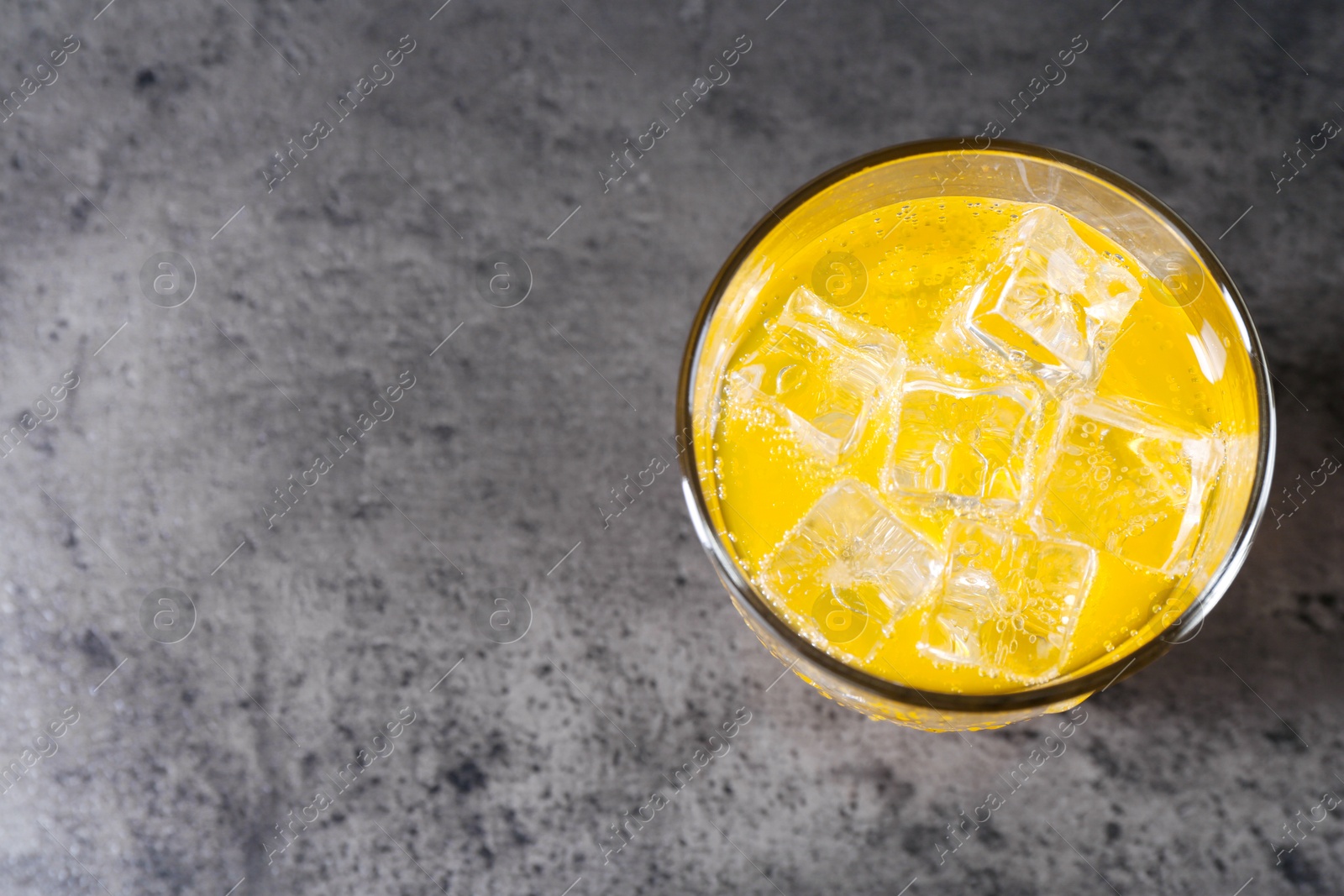 Photo of Sweet soda water with ice cubes in glass on grey table, top view. Space for text