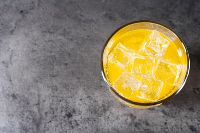 Photo of Sweet soda water with ice cubes in glass on grey table, top view. Space for text