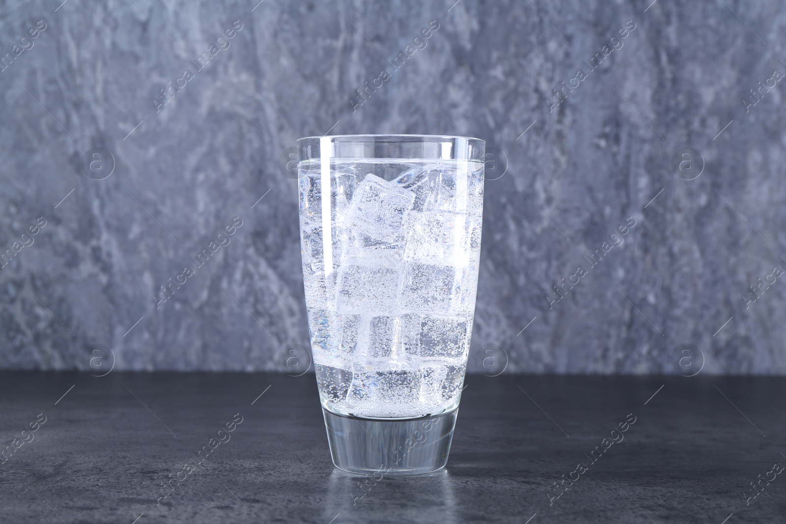 Photo of Refreshing soda water with ice cubes in glass on grey table