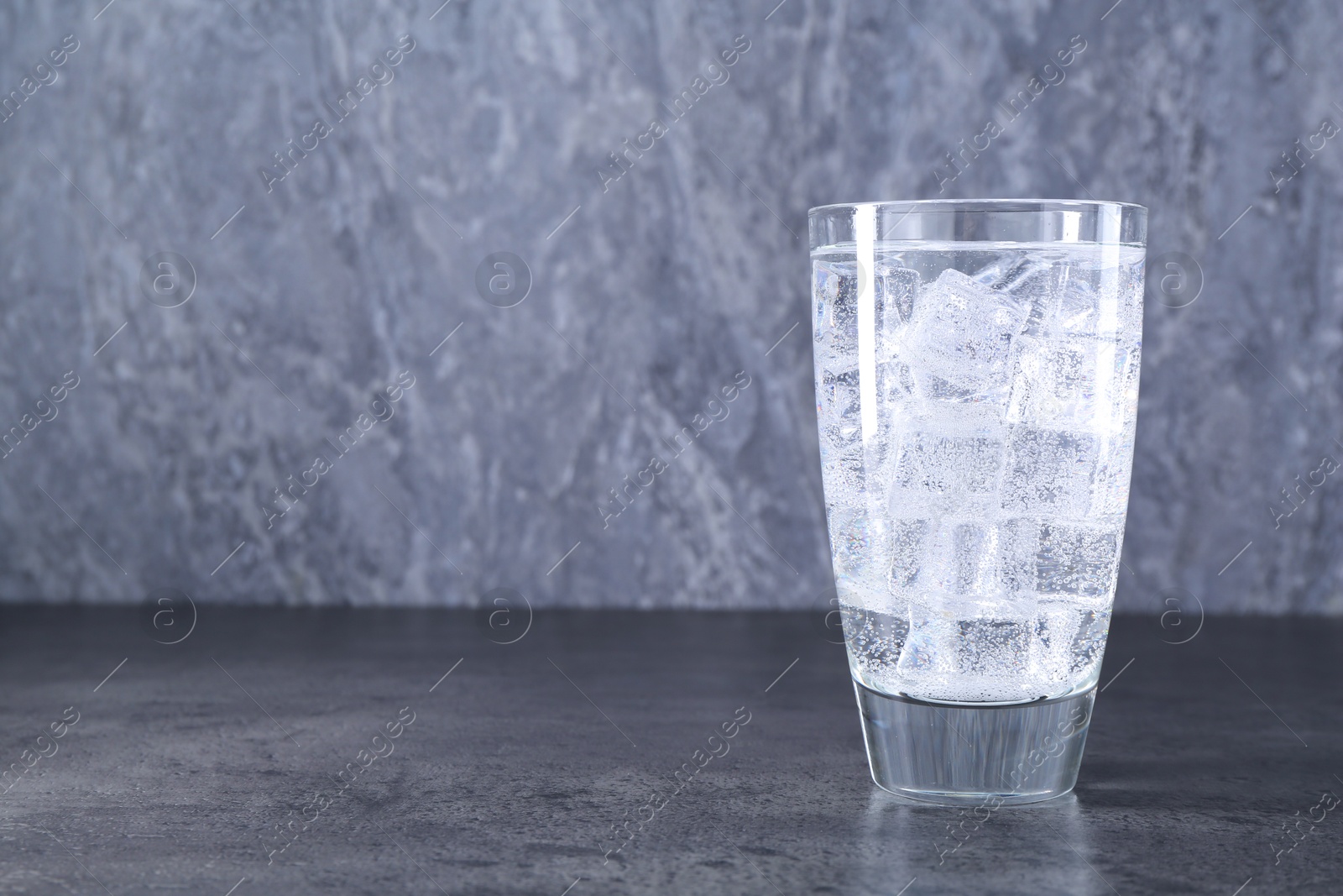 Photo of Refreshing soda water with ice cubes in glass on grey table, space for text