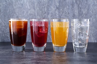 Photo of Sweet soda water of different flavors with ice cubes in glasses on grey table