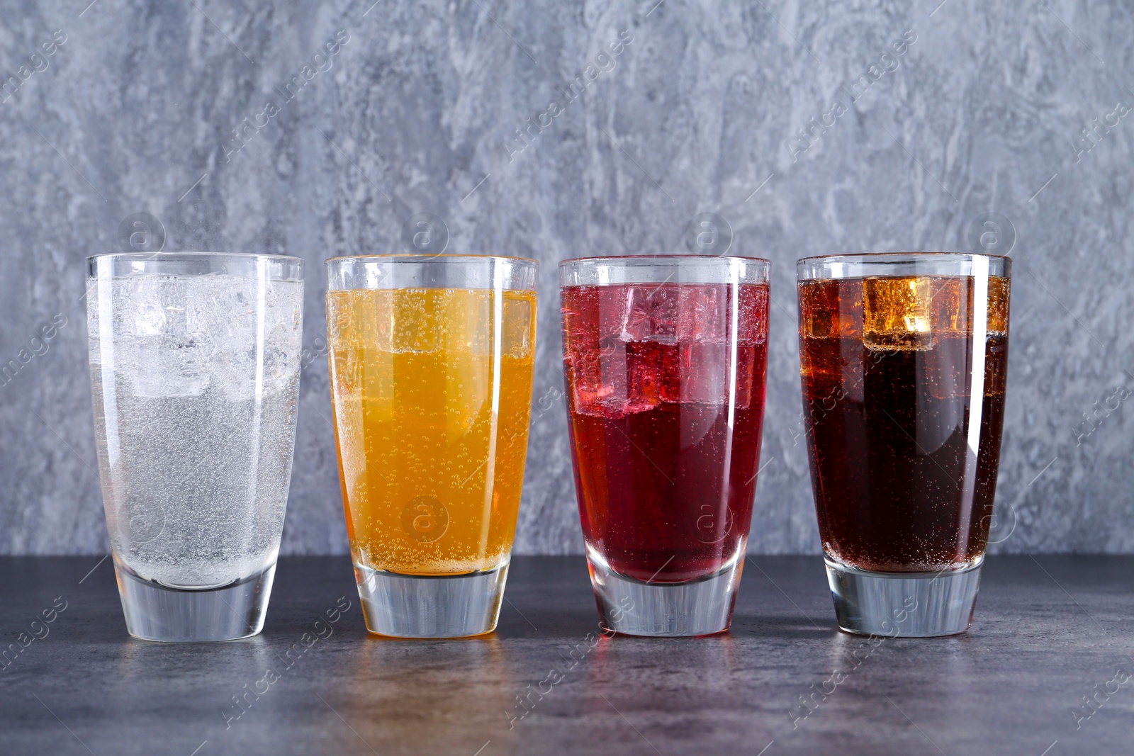 Photo of Sweet soda water of different flavors with ice cubes in glasses on grey table