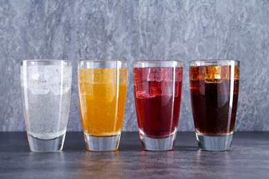 Photo of Sweet soda water of different flavors with ice cubes in glasses on grey table