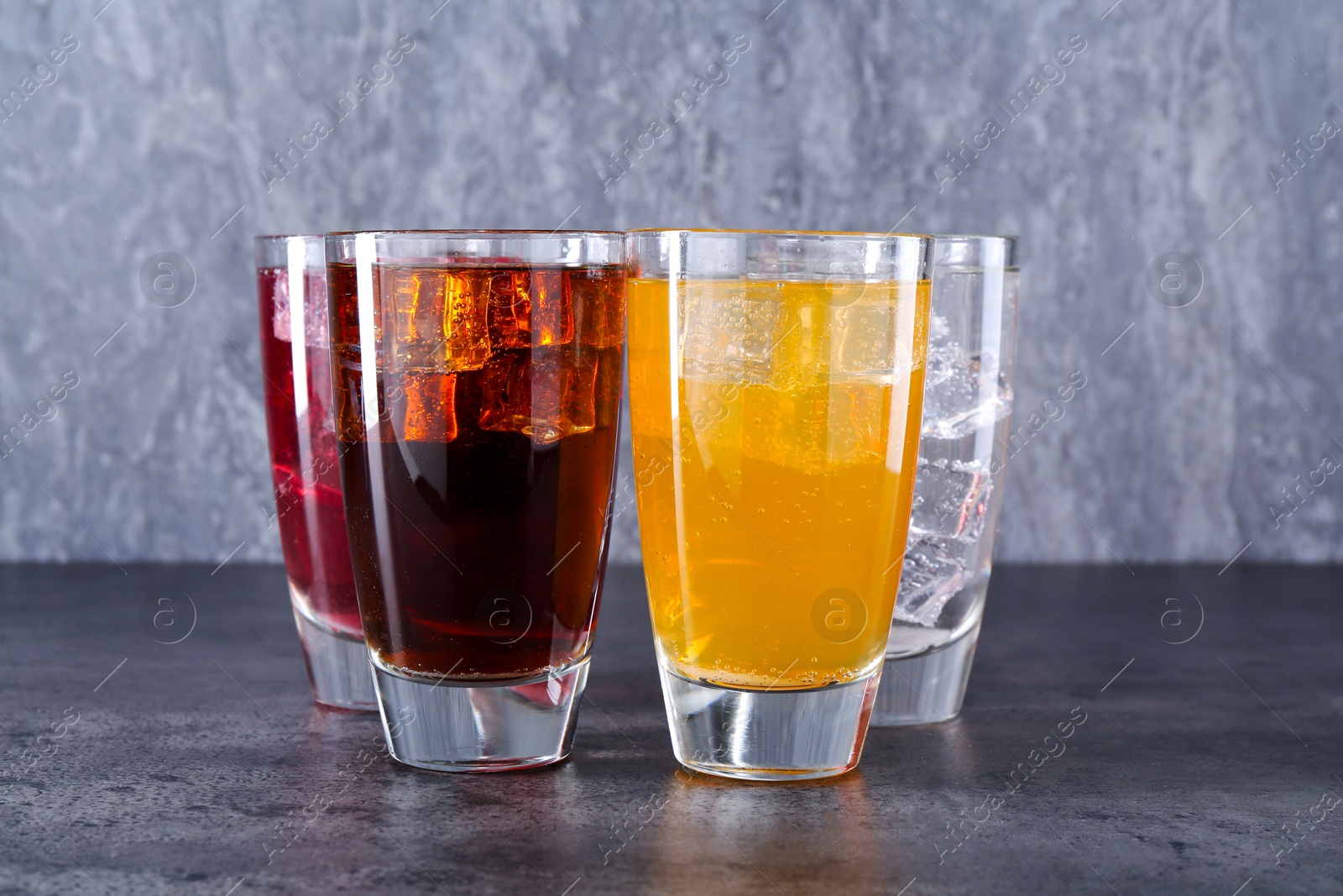 Photo of Sweet soda water of different flavors with ice cubes in glasses on grey table