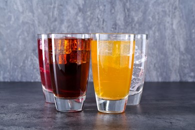 Photo of Sweet soda water of different flavors with ice cubes in glasses on grey table