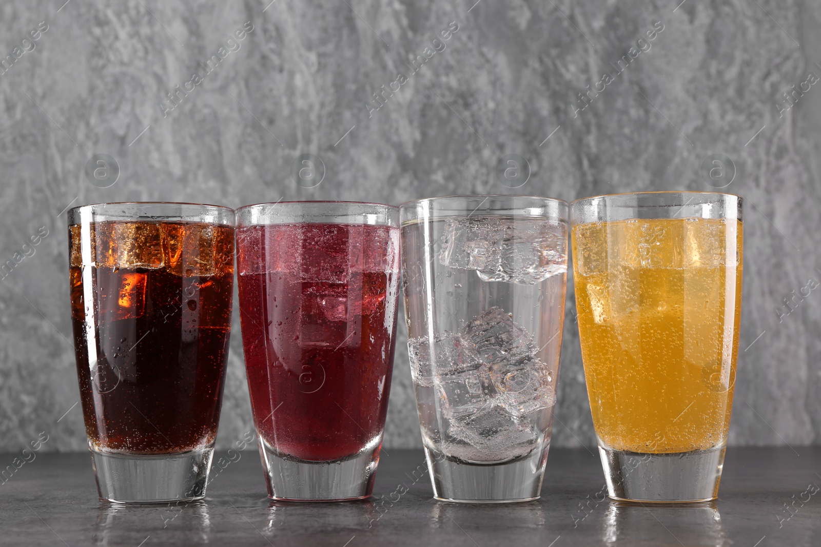 Photo of Sweet soda water of different flavors with ice cubes in glasses on grey table