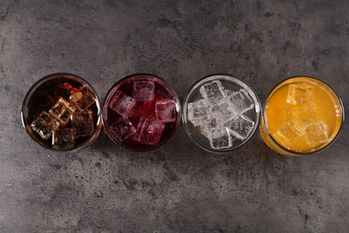 Photo of Sweet soda water of different flavors with ice cubes in glasses on grey table, flat lay